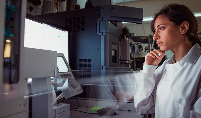 Female scientist looks at a computer monitor next to research equipment
